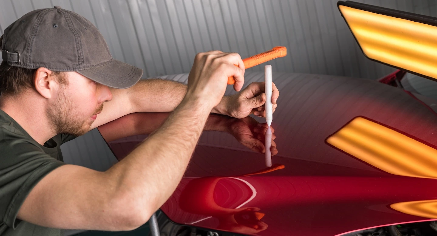 Technician using Paintless Dent Repair to fix a minor dent on a car hood.
