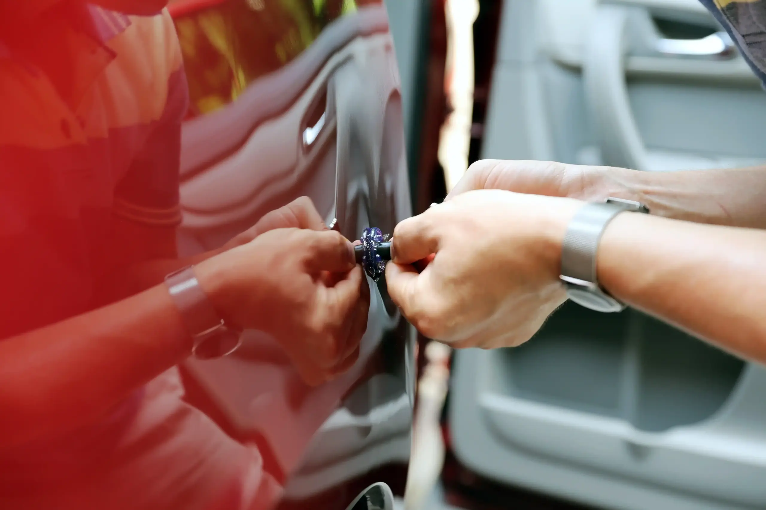 Technician using a PDR tool to repair a door ding on a red vehicle