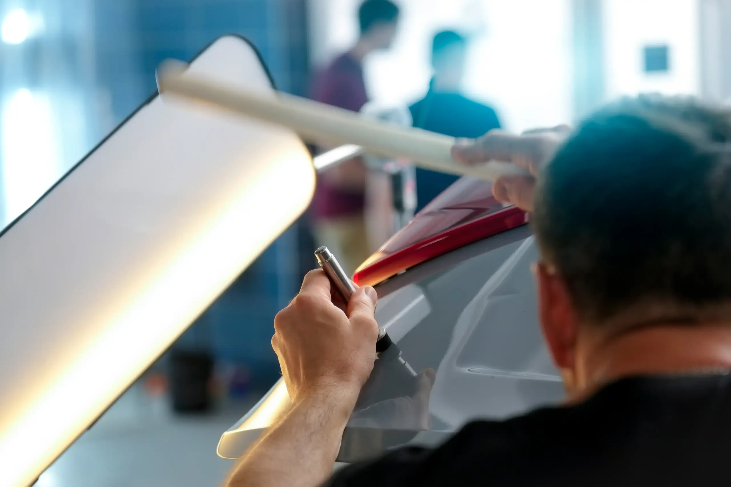 Technician using a PDR light board to inspect a car panel for dents