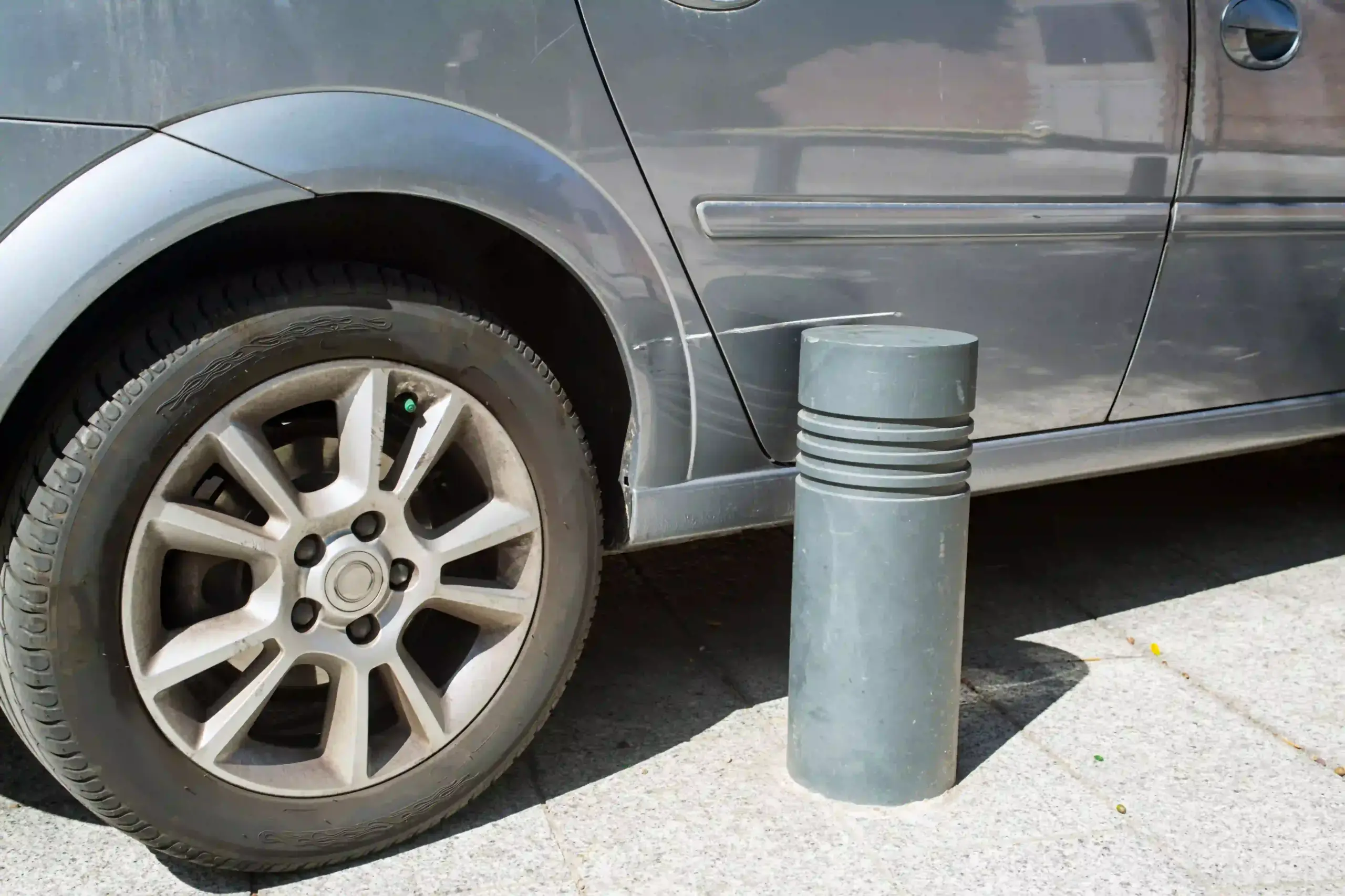 Close-up of a dent and scratch on a gray car's rear panel caused by a parking lot bollard