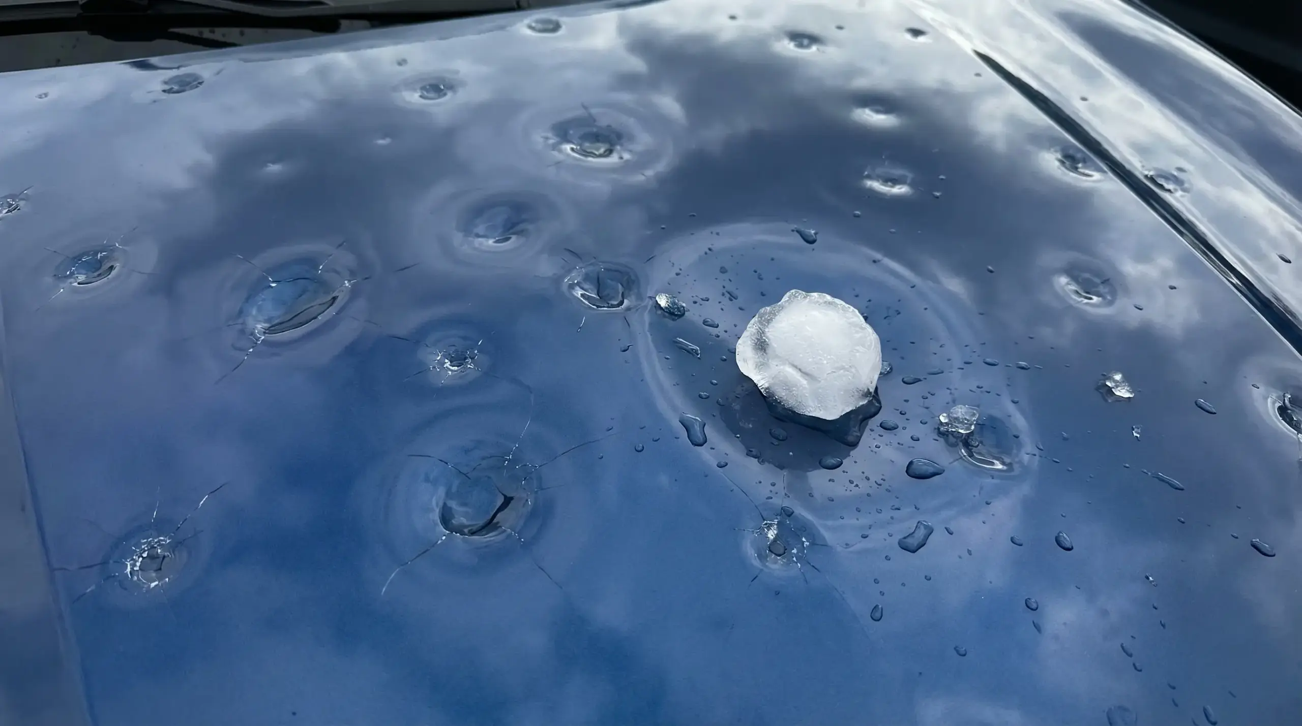 Multiple hail dents on a car's hood near the windshield
