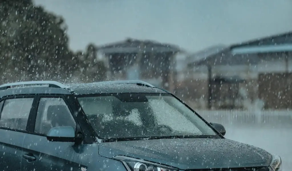 A car parked outside during a hailstorm, hail striking the windshield and hood 