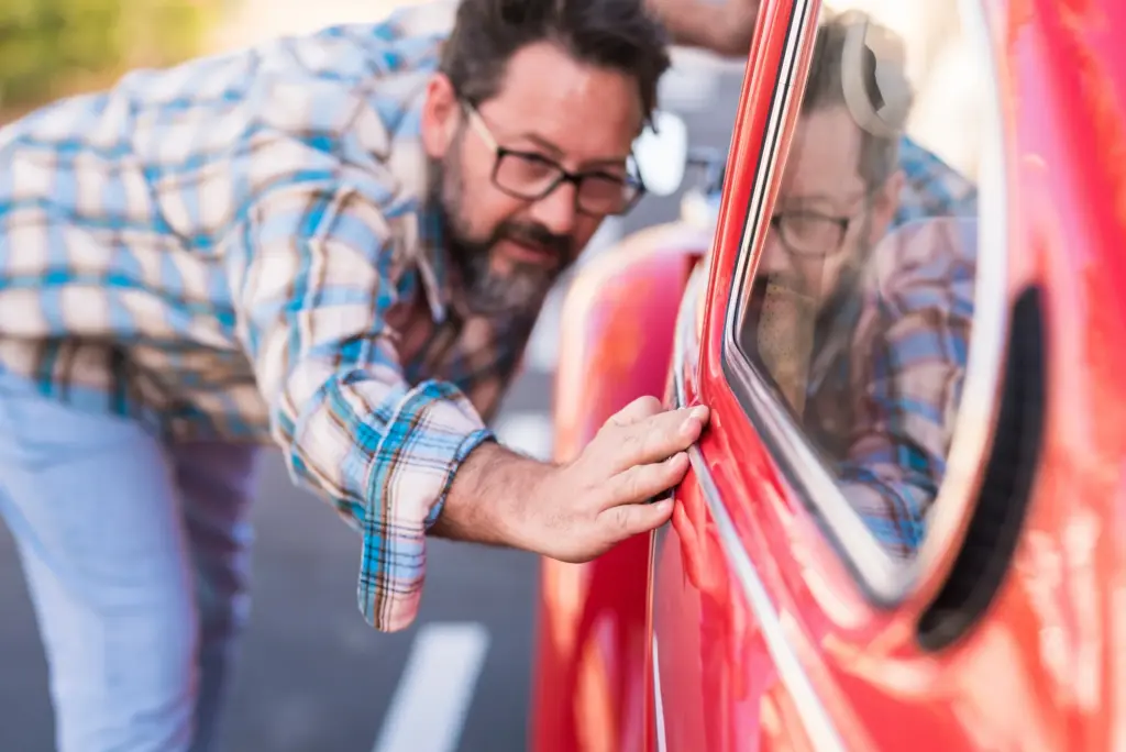 A man closely inspecting a dent along a car's door panel