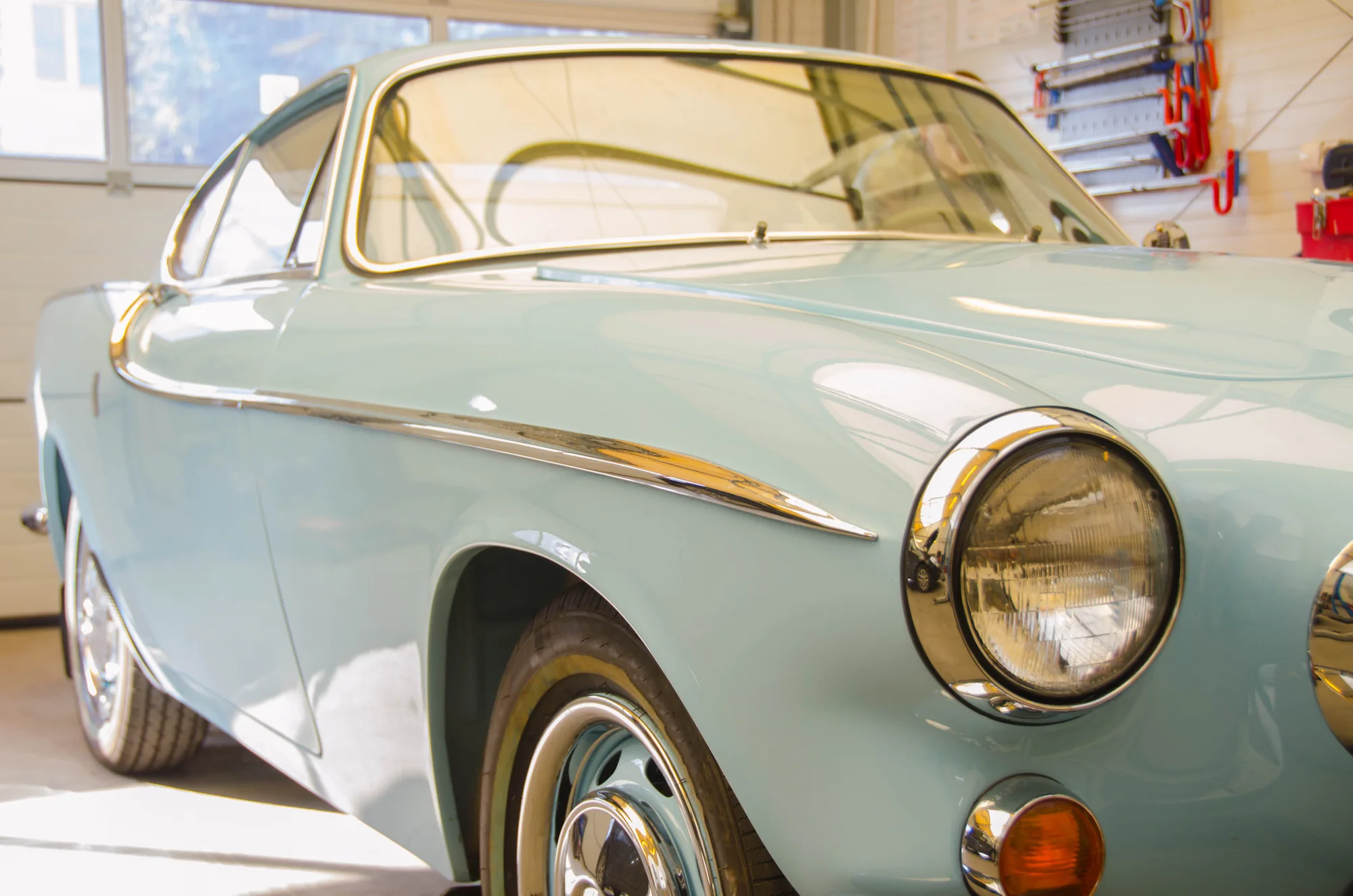 Light blue classic coupe parked in a garage, front three-quarter view 